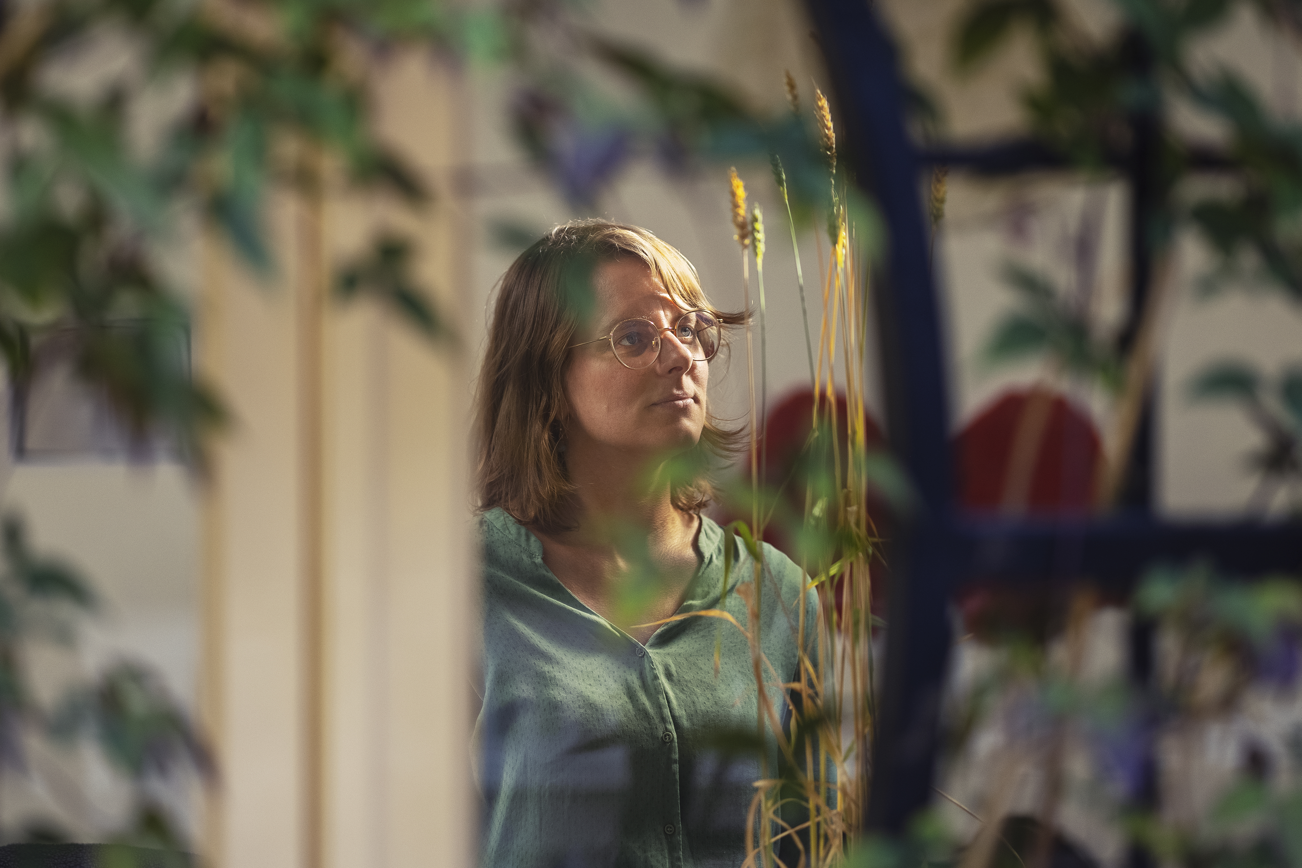 Janneke Kornet door het raam van het atelier gezien met groen ervoor